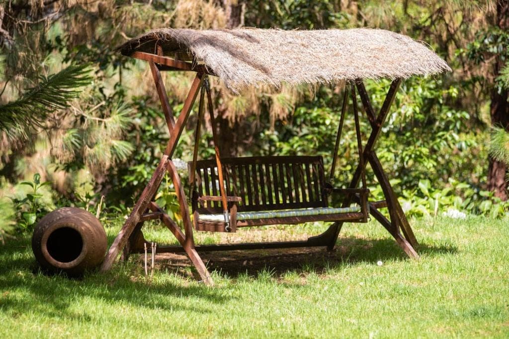Banco columpio con techo de brezo sobre el césped del jardín de El Castaño, junto a una tinaja de barro