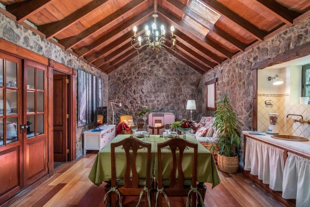 Salón de El Castaño bajo el techo abovedado de vigas de madera, con pared de piedra volcánica