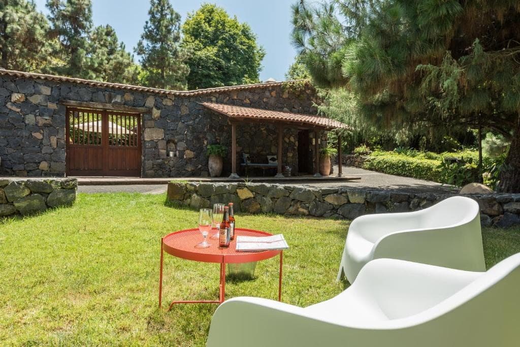 La Era, una de las casas de piedra de la finca, con una mesa roja y dos sillones blancos en el césped