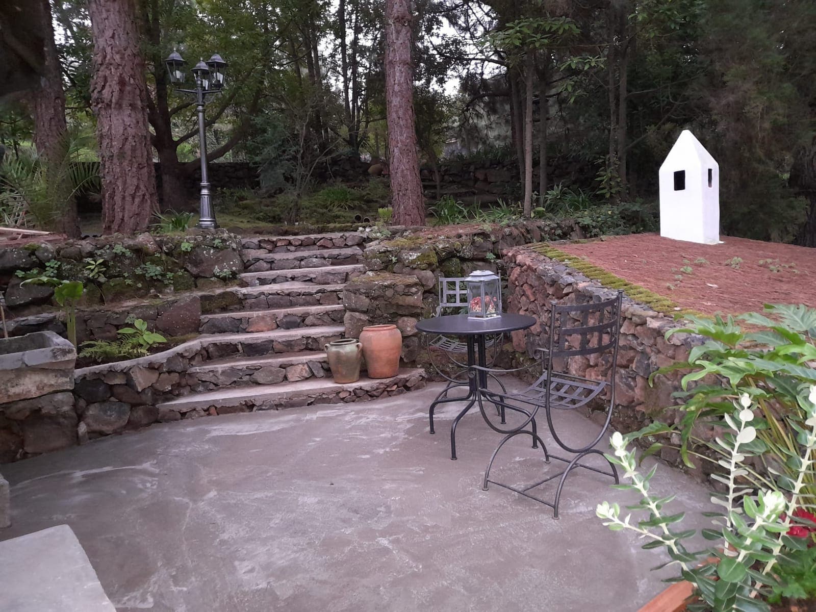 Rincón empedrado del jardín junto al pajar, con mesa de hierro y escalones de piedra