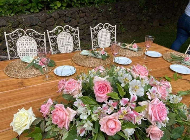 Detailaufnahme eines Hochzeitstisches mit zartrosa Blumen und weißen Stühlen im Garten des Anwesens
