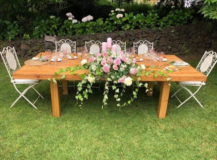 Mesa rectangular larga con velas rosas, ramo de flores y servilletas atadas con espigas
